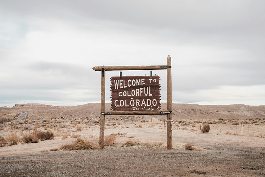 A wooden sign in the desert with the words Welcome to Colorful Colorado