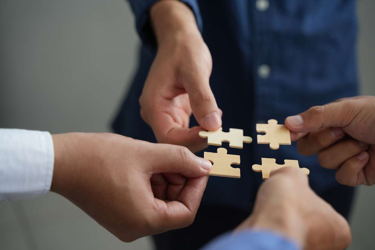 Hands of four people put together a jigsaw puzzle