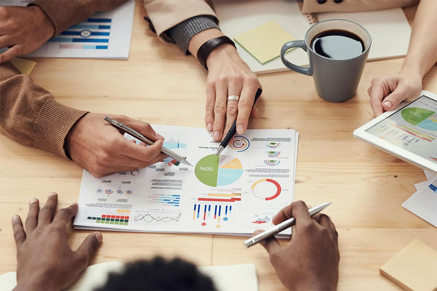 Close-up of hands of four people collaborating on a project and reviewing charts and graphs